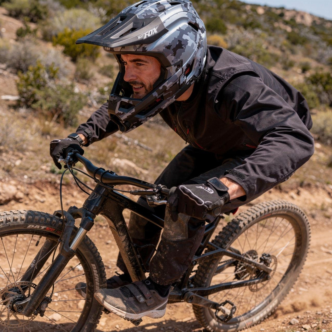 Pilote de VTT de descente en pleine accélération portant le casque intégral édition Shadow camouflage gris, équipé de gants et d'une tenue technique noire.